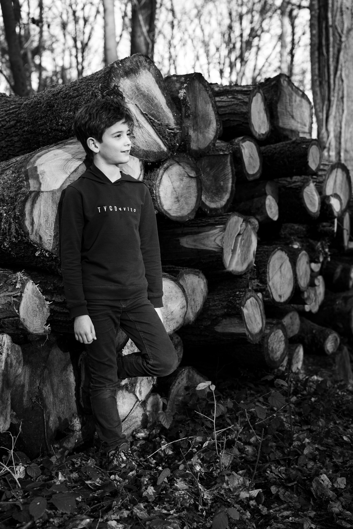 Boy posing against stack of wood, black and white